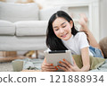 Woman laying down playing with tablet in living room, relaxation concept, lifestyle 121888934