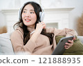 Asian freelance woman using headphones and tablet sitting on sofa at home happily, technology and work concept, everywhere is internet 121888935
