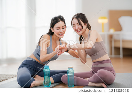 Two Asian women looking at smartwatches to measure their physical fitness during a break from exercise, health and wellness concept, exercise 121888938