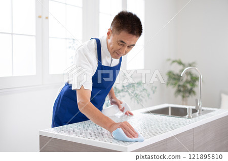 Senior male housekeeper cleaning the kitchen Senior male housekeeper cleaning the kitchen 121895810