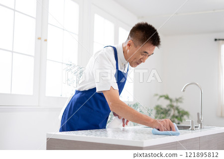 Senior male housekeeper cleaning the kitchen 121895812