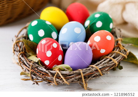 Colorful Easter eggs in a basket on white wooden table. 121896552