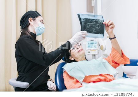 Dentist showing x-ray to patient, patient looking at x-ray with dentist, dental patient holding her x-ray, a dentist with x-ray examination 121897743