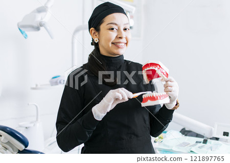 Smiling female dentist showing a denture, Dentist explaining tooth brushing, female dentist showing a denture and brush 121897765