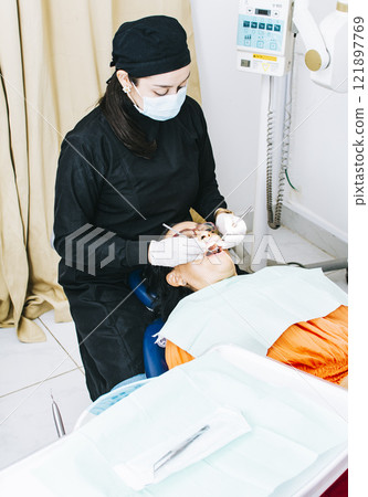 Dentist with patient lying down, Dentist examining mouth to patient, Woman dentist doing endodontics to woman patient, Dentist performing stomatology Dentist with patient lying down, Dentist examining mouth to patient, Woman dentist doing endodontics to woman patient, Dentist performing stomatology 121897769