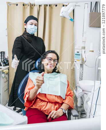 Dentist with thumb up patient in office, Woman shows thumb up sitting in dentist office, Dentist and satisfied patient with thumb up 121897779