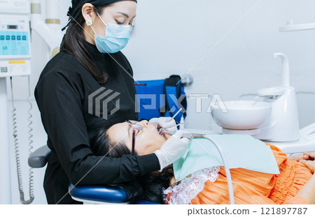 The stomatologist cleaning a patient's teeth, a dentist cleaning a patient's mouth, a dentist cleaning a patient's caries, a dentist cleaning a patient's mouth 121897787