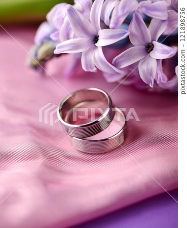 AI generative image of two simple design of titanium wedding rings on pink background with hyacinth. Shallow depth of field, close up the wedding ring with space. Vertica; image. AI generative image of two simple design of titanium wedding rings on pink background with hyacinth. Shallow depth of field, close up the wedding ring with space. Vertica; image. 121898756