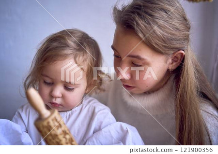 a family with two daughters, a teenager and a toddler, cook cookies together in the kitchen, sisterly love 121900356