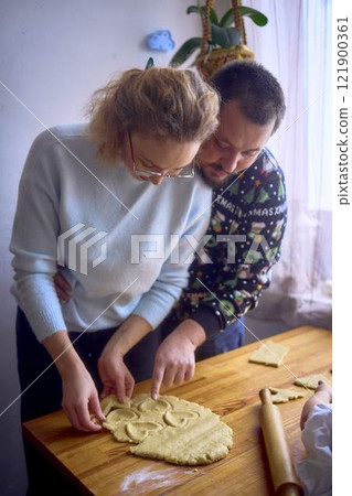 a husband and wife are cooking Christmas cookies in the kitchen 121900361