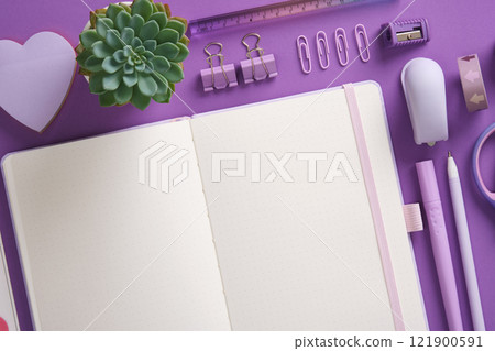 Open notepad and stationery, felt-tip pens, stapler, ruler, eraser, pins, clips in purple theme. Space for your text. 121900591