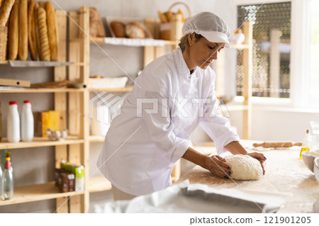 Working in bakery - woman kneads raw dough to make baguettes or croissants Working in bakery - woman kneads raw dough to make baguettes or croissants 121901205