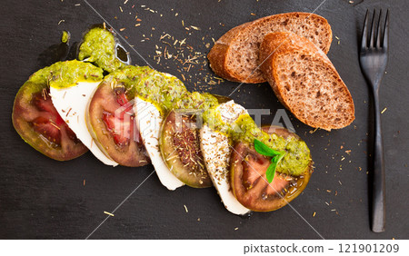 Caprese salad with mozzarella, black tomatoes and pesto on black stone plate Caprese salad with mozzarella, black tomatoes and pesto on black stone plate 121901209