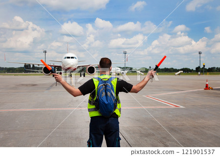 The traffic controller at the airport shows the semaphore with sticks to the pilot of the plane where to park. Arrival of the plane on the runway. Handling service. 121901537