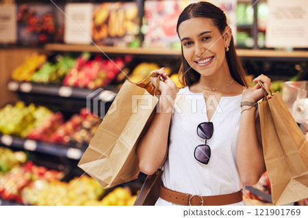 Grocery shopping, food and diet with a young woman in a retail, convenience store or grocer and fruit and vegetables in the background. Portrait of a female with paper bags in a fresh produce aisle 121901769