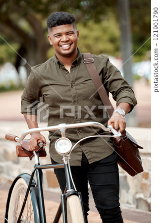 Happy business man riding a bicycle, commuting and staying active while traveling in city. Portrait of a smiling, cheerful and positive guy cycling on a bike and being carbon neutral at a park 121901790
