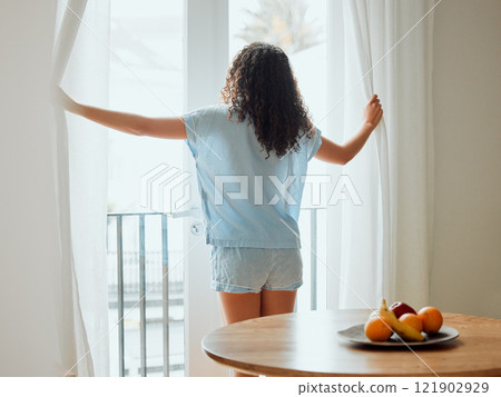 Awake, waking up and fresh new day or morning for a young woman opening the curtains. Back view of a carefree female with hope thinking while looking out the window in her house or at home Awake, waking up and fresh new day or morning for a young woman opening the curtains. Back view of a carefree female with hope thinking while looking out the window in her house or at home 121902929
