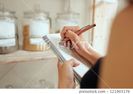 Entrepreneur stock counting and writing or planning shopping list in a store on a notepad. Small business owner making a budget for inventory and restocking of supplies in local store, shop or cafe 121903176