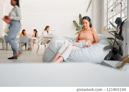 Serious, young design student relaxing and reading or listening to music in break room in startup office, with colleagues. Modern creative designer working on tablet in casual informal business Serious, young design student relaxing and reading or listening to music in break room in startup office, with colleagues. Modern creative designer working on tablet in casual informal business 121903190