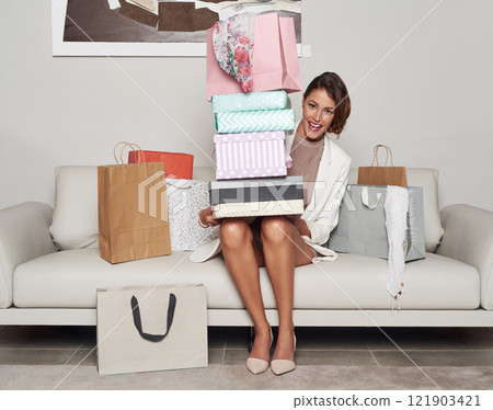 Excited, trendy and fashionable woman holding shopping bags while sitting on a sofa portrait. Rich, smiling and stylish elegant female at home after buying retail clothing items on sale or discount 121903421
