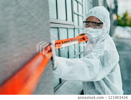 Covid healthcare worker responding to a biohazard in a public area using barrier tape outside. First responder in protection hazmat suit and mask separating a space due to a new pandemic or outbreak 121903426