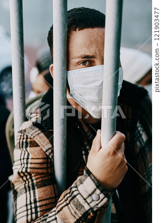 Sick, refugee of a young covid patient in quarantine to cross the border with a medical face mask. Foreign man in a prison crowd during a pandemic following healthcare safety rules of the virus. Sick, refugee of a young covid patient in quarantine to cross the border with a medical face mask. Foreign man in a prison crowd during a pandemic following healthcare safety rules of the virus. 121903477