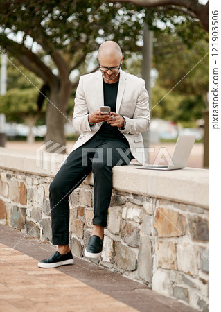 Stylish, cool smiling businessman on a phone in the park outside in nature. Happy man texting, chatting or reading social media messages on a smartphone outdoors on a break from work with copy space 121903506