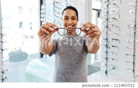 Female holding pair of trendy new glasses, stylish spectacles and prescription lenses at an optometrist. Portrait of a customer choosing, buying and shopping for frames for better vision and eyesight Female holding pair of trendy new glasses, stylish spectacles and prescription lenses at an optometrist. Portrait of a customer choosing, buying and shopping for frames for better vision and eyesight 121903552