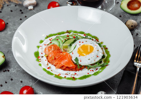 Poached eggs on top of smashed avocado on sourdough toast with smoked salmon. Healthy breakfast with plate on table. Top view. Copy space to right  121903634