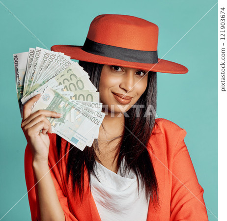 Rich, successful and wealthy young woman holding cash money after winning competition, lottery or casino prize. Smiling, elegant and trendy female with pay reward against a blue studio background 121903674
