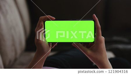 Young woman lying on a couch and using smartphone with horizontal green screen Young woman lying on a couch and using smartphone with horizontal green screen 121904316