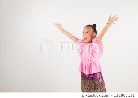 Portrait Thailand kid girl smiling traditional Thai dress costume raises fists in celebration of her success, studio isolated white background, kindergarten child saying yes with excitement winning 121905131