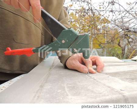 craftsman holding a clamp and a riveter and metal material for fixing parts, working with fasteners and a riveting gun on iron 121905175