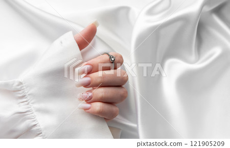 Woman showing stylish pastel pink manicure and silver ring on white silk fabric Woman showing stylish pastel pink manicure and silver ring on white silk fabric 121905209