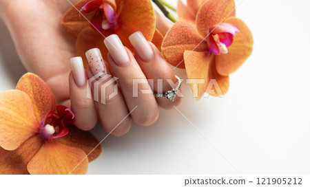 Woman hand showing stylish trendy nude manicure holding orange orchid flowers 121905212