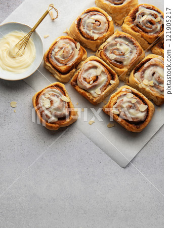 Freshly baked cinnamon rolls topped with cream cheese frosting and almond slivers 121905217