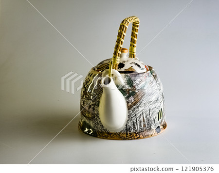 Front view. Ceramic teapot with abstract pattern and wicker straw handle on a white background. Front view. Ceramic teapot with abstract pattern and wicker straw handle on a white background. 121905376