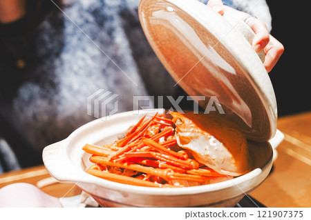 A young woman opening the lid of a crab pot [Photo courtesy of Seafood Izakaya Gyoruko] 121907375
