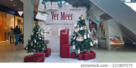 Festively decorated interior of the premises on New Year's Eve. In the hypermarket, banners with advertisements of trade brands are placed against the backdrop of a New Year tree. 121907575