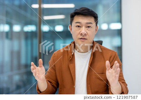 Serious focused man looking at camera close up, asian man talking using video call, businessman explaining at online business meeting conference. 121907587