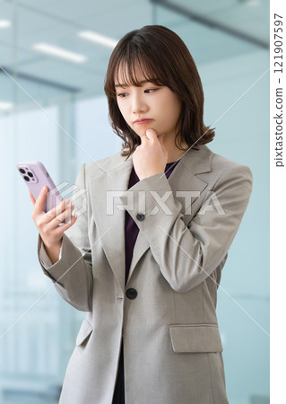 A young woman/businesswoman thinking while looking at her smartphone 121907597