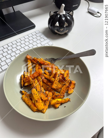 Plate of perfectly roasted vegetables seasoned with herbs, placed on a desk with a keyboard nearby. Concept of healthy eating during work breaks, blending productivity with mindful nutrition 121907665