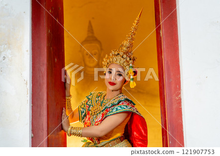 Woman with Khon mask charactor as angel stand in front of door frame of old building and look at camera with warm light in the background. Woman with Khon mask charactor as angel stand in front of door frame of old building and look at camera with warm light in the background. 121907753