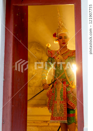 Vertical and wide shot image of man with Khon mask charactor as deity stand in front of door frame of old building with beam warm light in the background. Vertical and wide shot image of man with Khon mask charactor as deity stand in front of door frame of old building with beam warm light in the background. 121907755