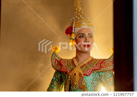 Close up shot of man with Khon mask charactor as deity stand with look to right side in front of door frame of old building with beam warm light in the background. 121907757