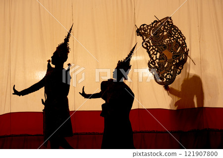 Silhouette and wide shot of man and woman with Khon or Mask dance costume stand with performance action in front of grand shadow play in the background with white screen. 121907800