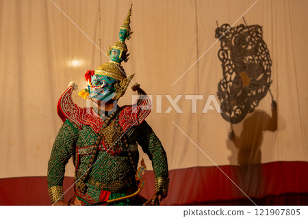 Close up man with Khon or Mask dance stand with performance action in front of grand shadow play in the background with white screen. 121907805