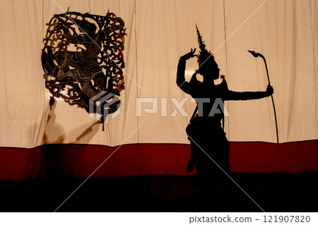 Silhouette of Khon or Mask dance player stand with performance action in front of grand shadow play in the background with white screen. Silhouette of Khon or Mask dance player stand with performance action in front of grand shadow play in the background with white screen. 121907820