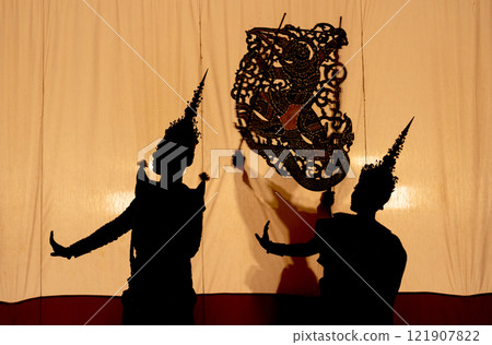 Close up silhouette of man and woman with Khon or Mask dance costume stand with performance action in front of grand shadow play in the background with white screen. 121907822