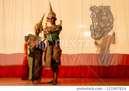 Two people of man and woman with Khon or Mask dance dress stand with performance action in front of grand shadow play in the background with white screen. 121907824